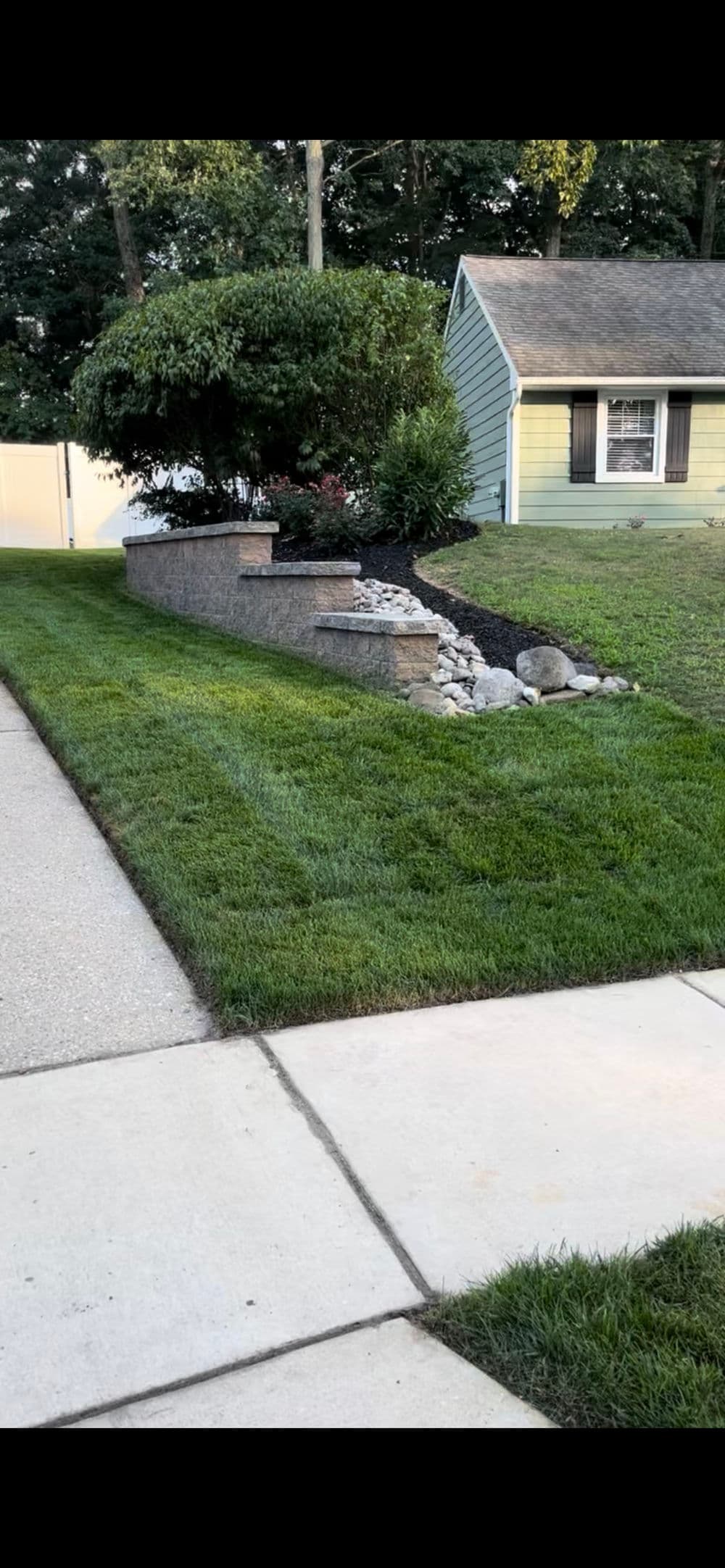 Landscaped yard with a stone wall, greenery, and well-maintained lawn next to a path.