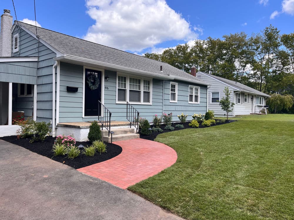 Light blue single-story home with landscaped yard and brick pathway. Perfect curb appeal.
