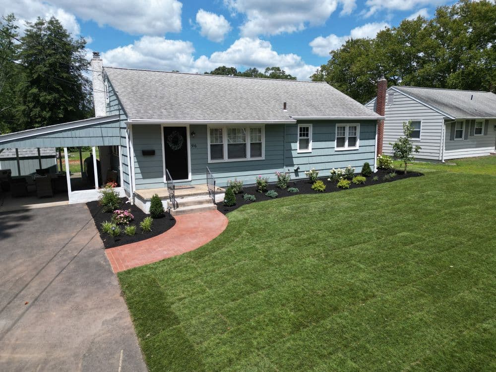 Single-story blue house with landscaped yard and patio under a bright sky.