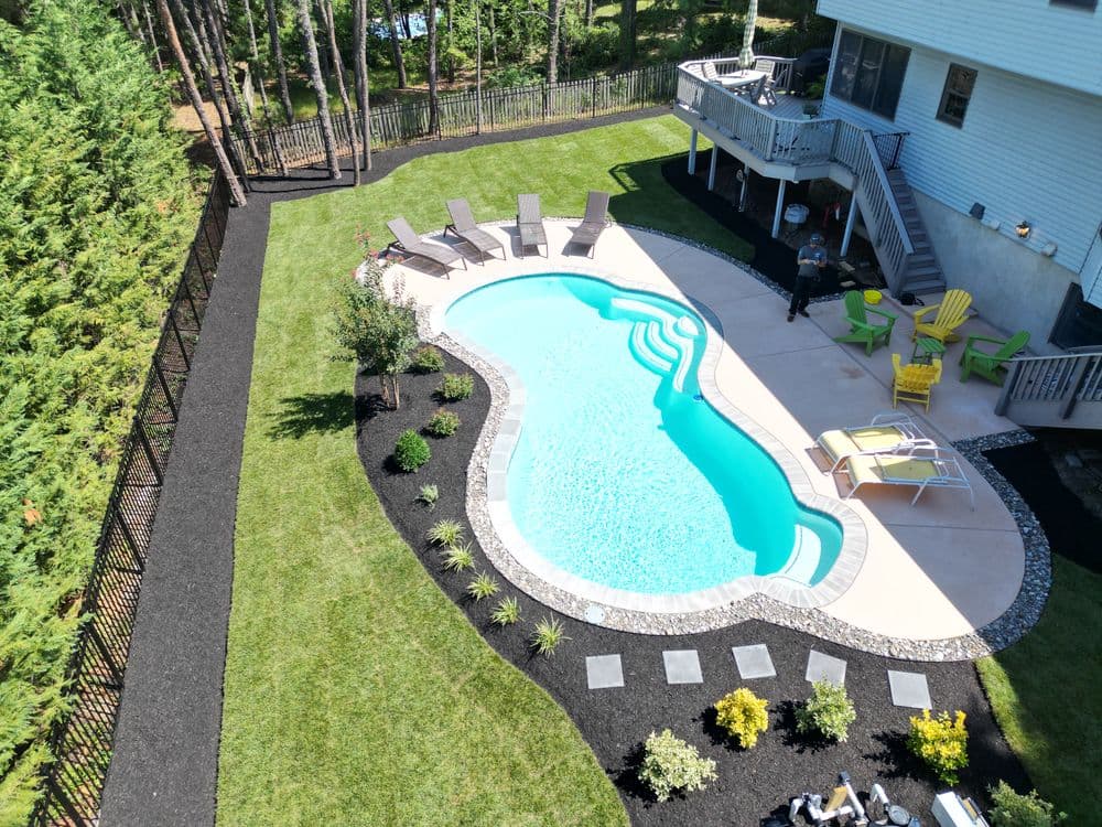 Backyard with a pool, lounge chairs, and greenery, showcasing a relaxing outdoor setting.