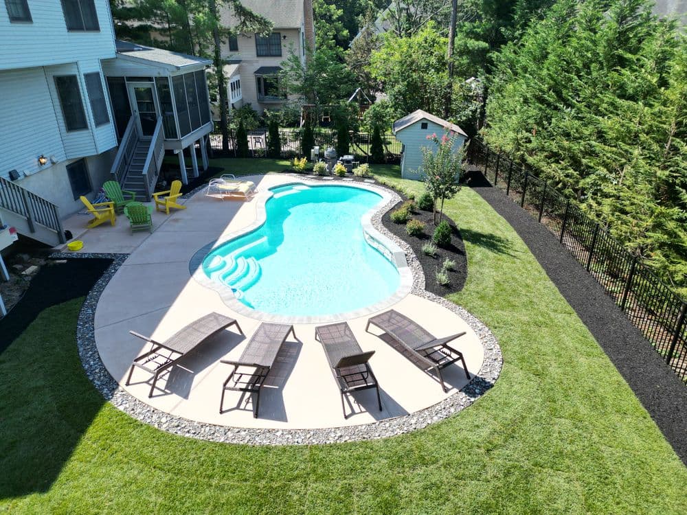 Aerial view of a landscaped backyard with a blue swimming pool, lounge chairs, and greenery.