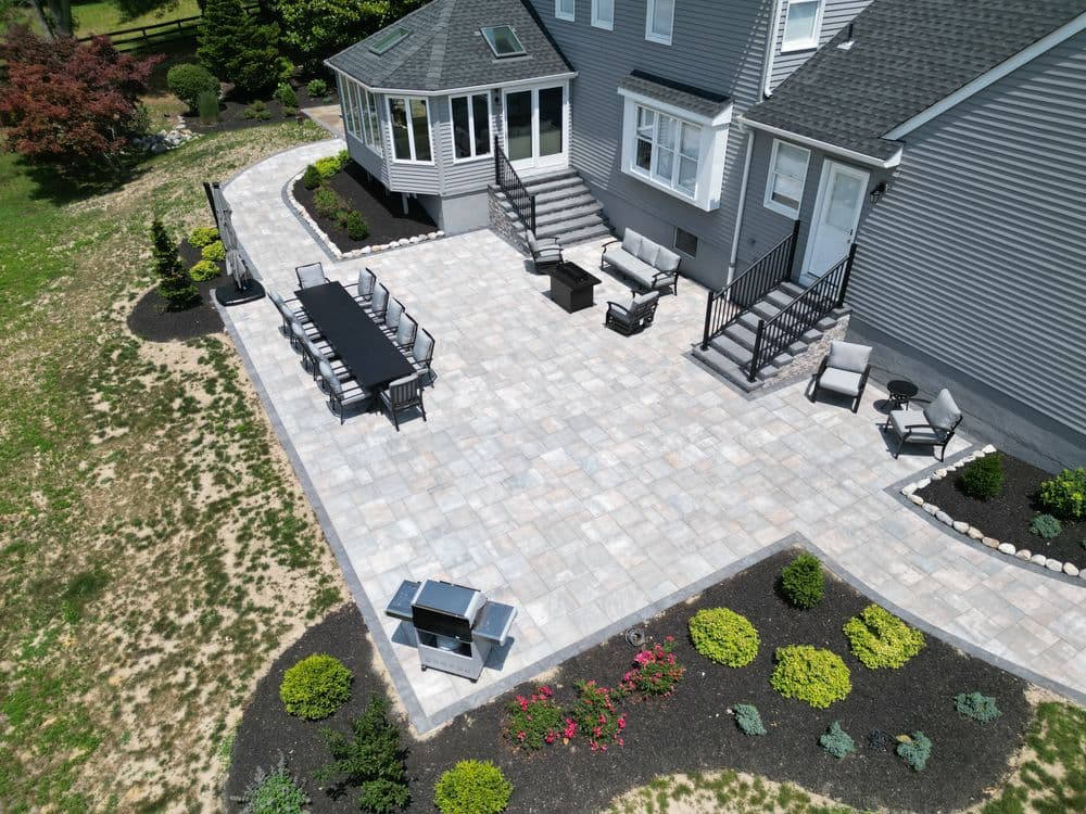 Drone view of a spacious patio with a dining set, BBQ grill, and landscaped garden.