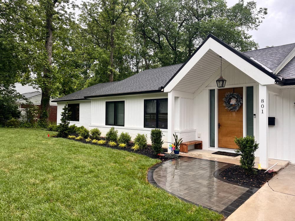 Modern white house with landscaped garden, black roof, and welcoming front porch.