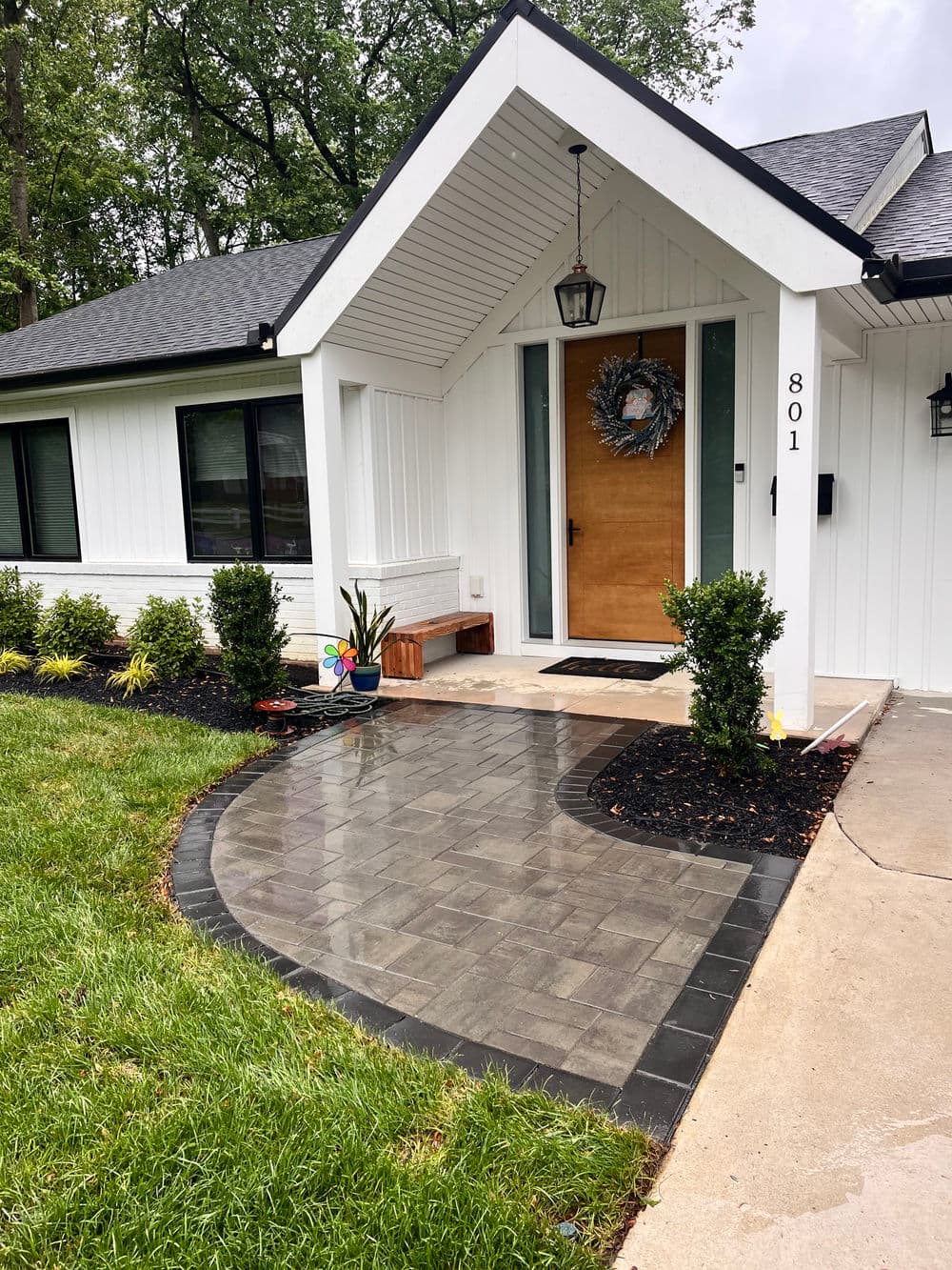 Modern home entrance with a wooden door, landscaped path, and greenery.