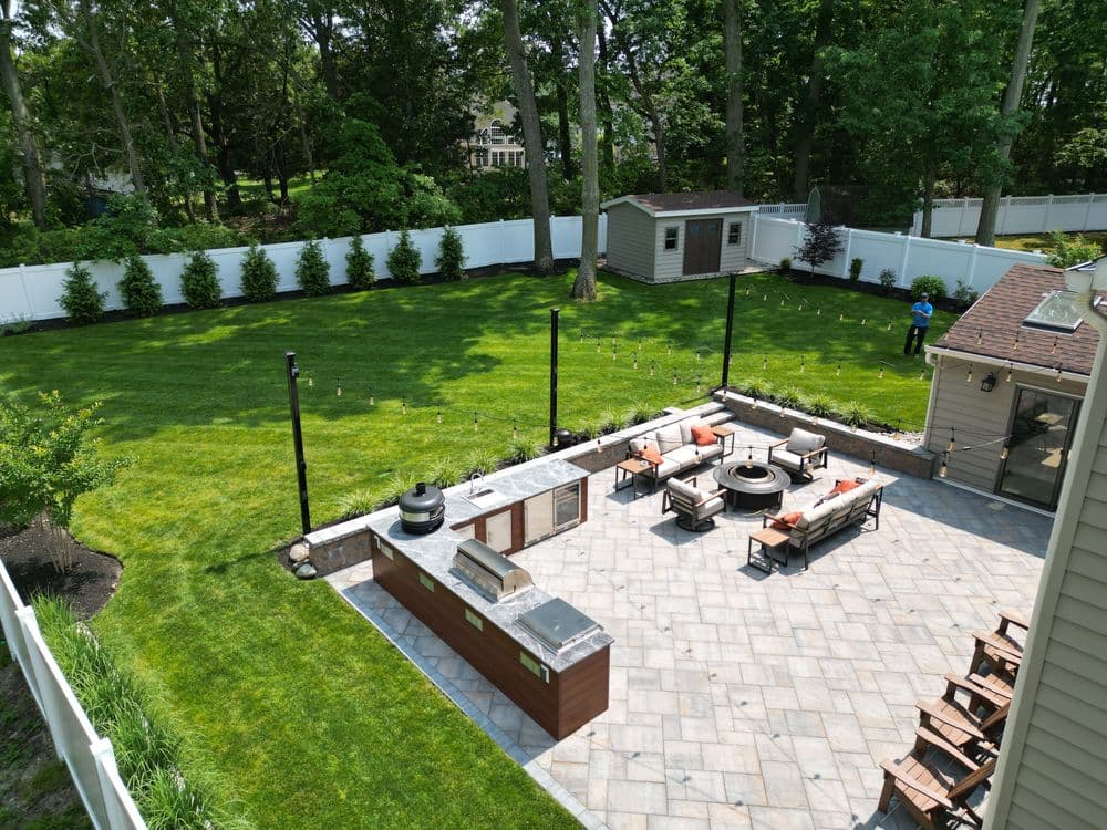Aerial view of a landscaped backyard with an outdoor kitchen, patio, and fire pit.
