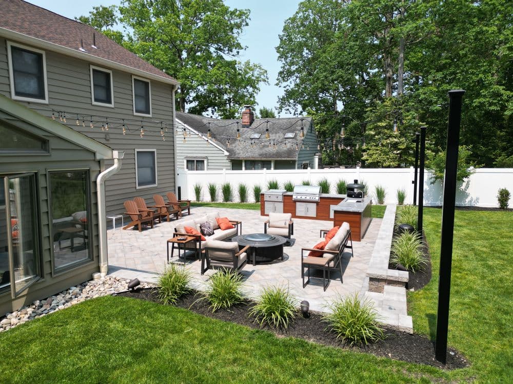 Backyard patio with seating area, fire pit, grill, and lush landscaping in a serene setting.