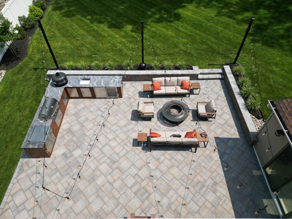 Spacious outdoor patio with fire pit, seating, grill, and string lights in a lush garden setting.