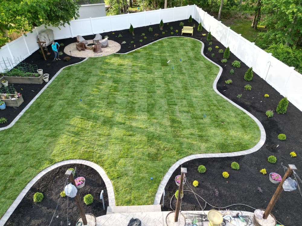Lush green lawn with landscaped garden beds and seating area in a backyard setting.