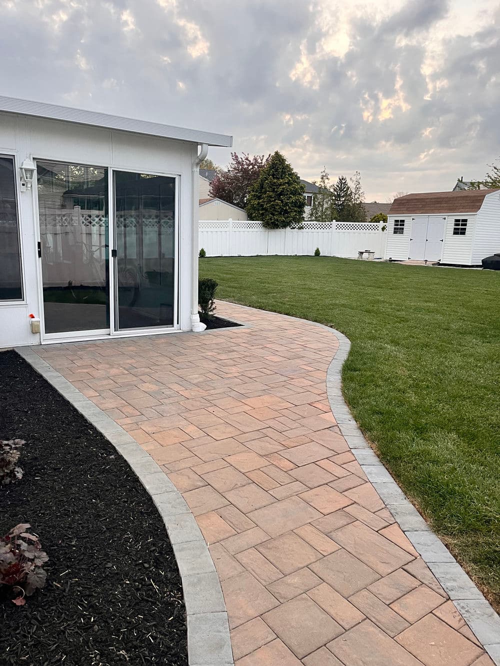 Curved brick pathway leading to green lawn and modern white home exterior.