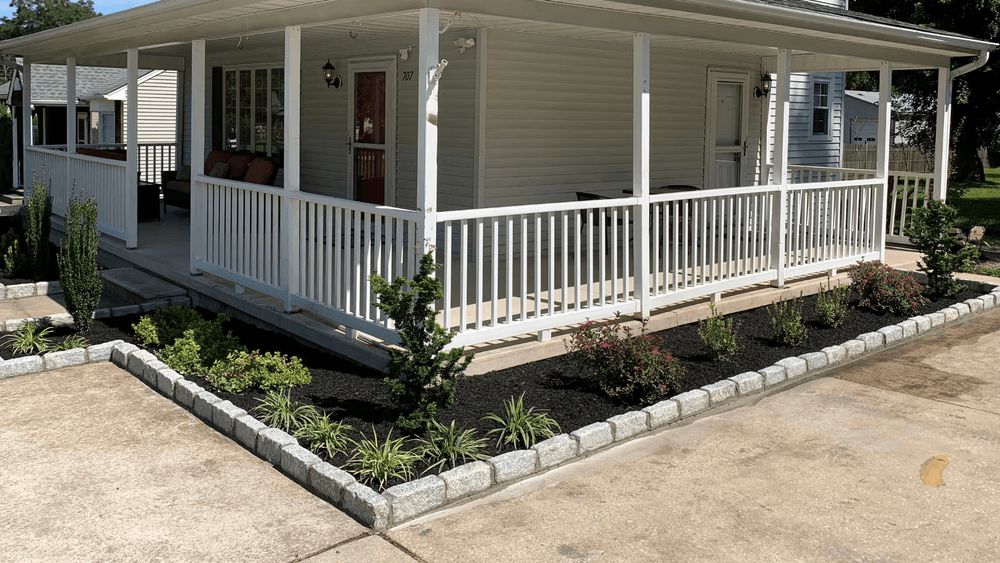 House porch with white railing, landscaped garden, and fresh mulch in front yard.