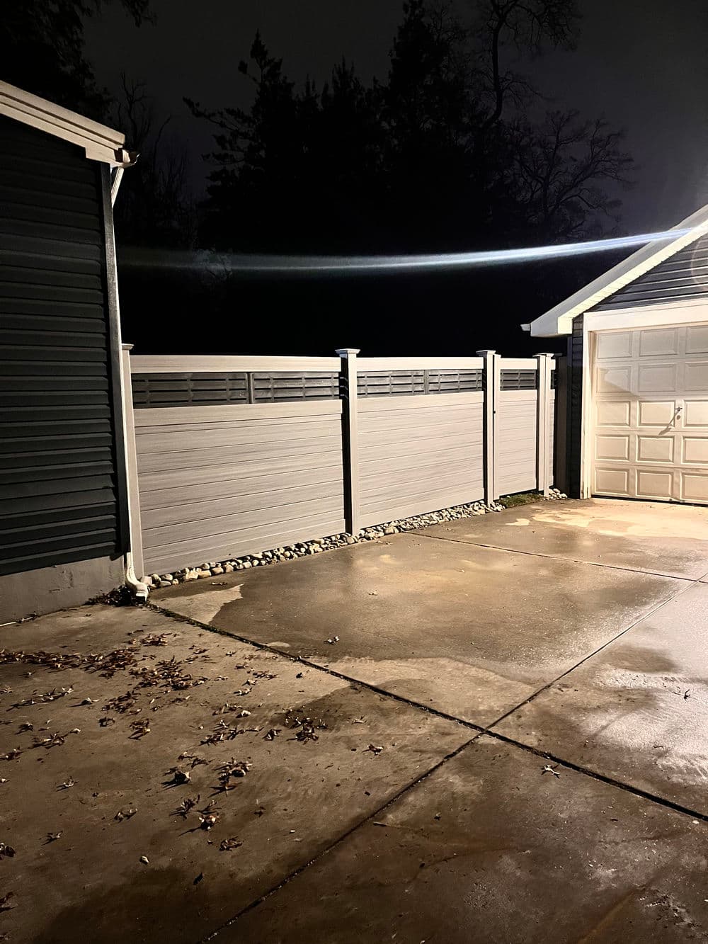 Illuminated driveway at night with a fenced area and garage in the background.