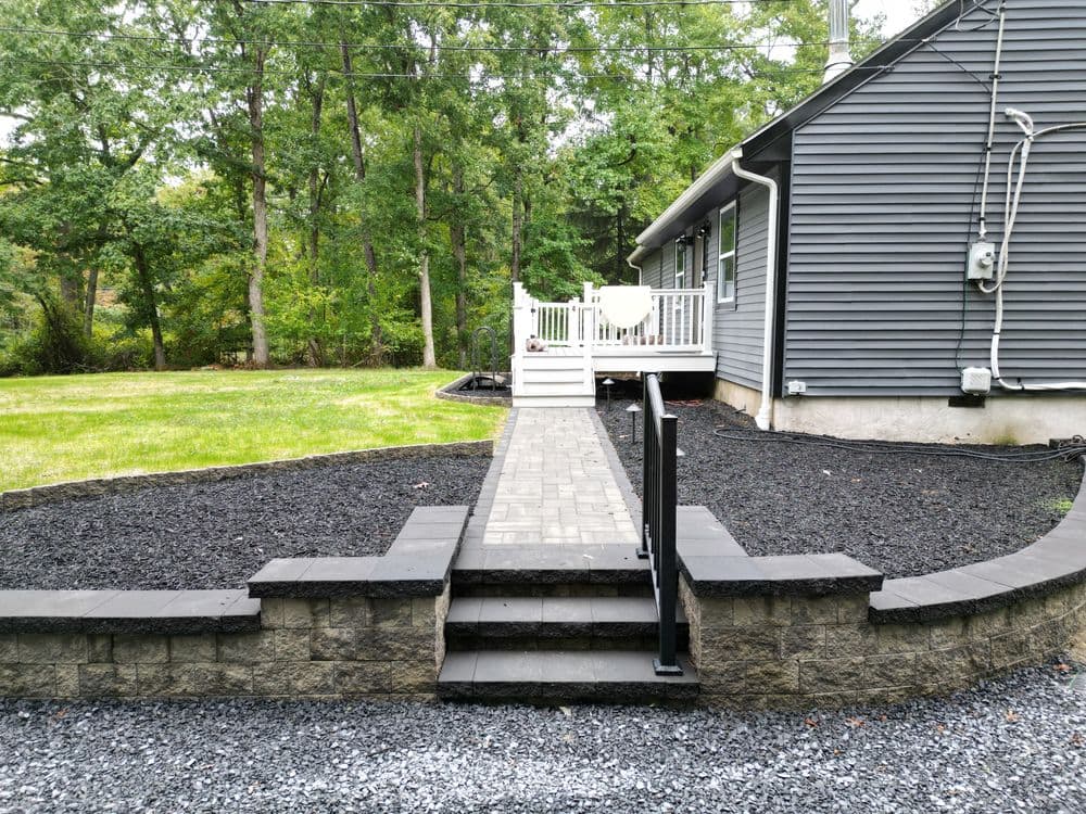Stylish backyard with a stone pathway, black mulch, and a deck leading to a gray house.
